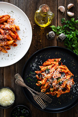 Penne noodles with tomato sauce, black olives and parmesan cheese served on wooden table	