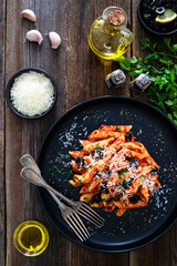 Penne noodles with tomato sauce, black olives and parmesan cheese served on wooden table	