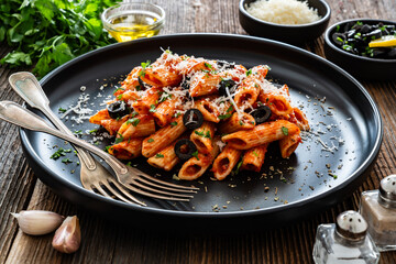 Penne noodles with tomato sauce, black olives and parmesan cheese served on wooden table	