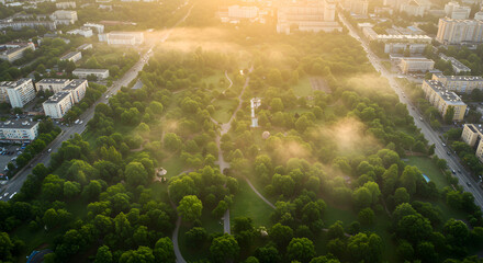 High Angle Shot of Green City Park with Dense Trees and Early Morning Fog at Sunrise and Cars on Roads
