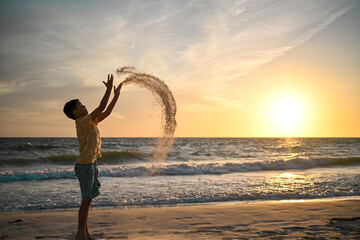 Boy throws sand with curved effect and sunset over ocean