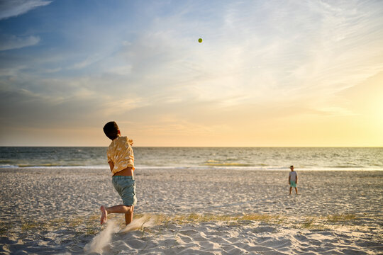 Boy throws ball to brother with beautiful sunset over the ocean