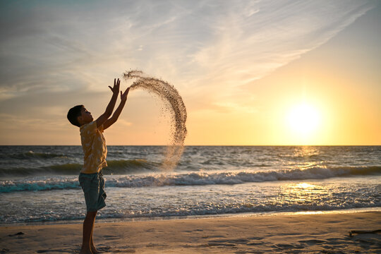 Boy throws sand with curved effect and sunset over ocean