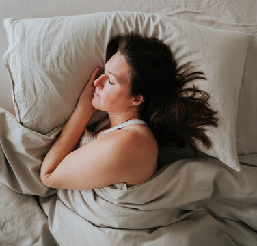 Overhead view of woman sleeping in bed on beige bedding.