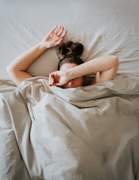 Top view of tired woman in bed with arm over head and covering eyes.