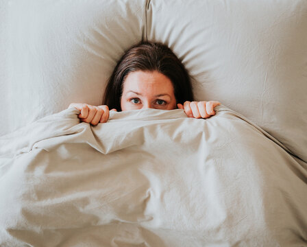 Top view of woman in bed hiding under covers with blanket over face.