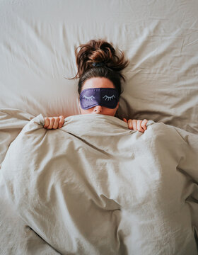Top view of woman in bed hiding under covers with blanket over face.