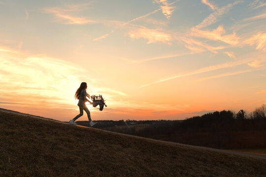 Side view tween girl riding stick horse outdoors beautiful sunse