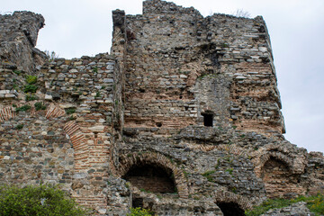 A stunning view of old stone walls from an ancient castle surrounded by nature. The historic ruins exhibit weathered textures, arched openings, and brick detailing against a serene, cloudy backdrop.