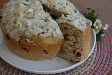 Sliced round sweet bread with almond and white chocolate glaze for Easter on a white tray on wooden table with wildflowers