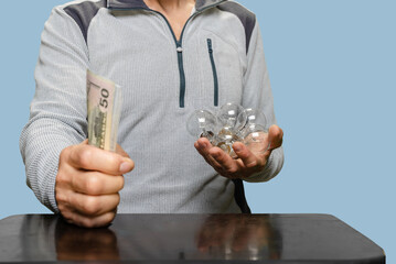 Closeup of man holding pack of dollars cash in one hand and incandescent lightbulbs in other hand, Man holding incandescent light bulbs and cash, highlighting the cost of electricity