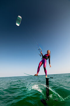Attractive woman riding hydrofoil surfboard using kiteboard or kitesurfing wing. Athletic girl smiling at camera during workout