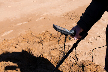 Beach treasure hunt. Adult using metal detector on sandy shore