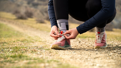Front view of an unrecognizable young adult caucasian woman tying shoe laces of running shoes getting ready for run. Female trail runner, jogging girl, cardio workout outdoor, health, fitness, nature