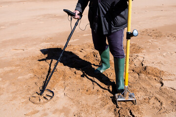 Adult using metal detector and shovel on beach sand for treasure hunting