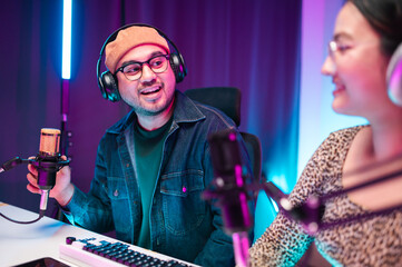 Teenagers, men and women, host podcasts in a room using LED lights, computers, headphones, condenser microphones, and tablets to share their knowledge and experiences through live online broadcasts.
