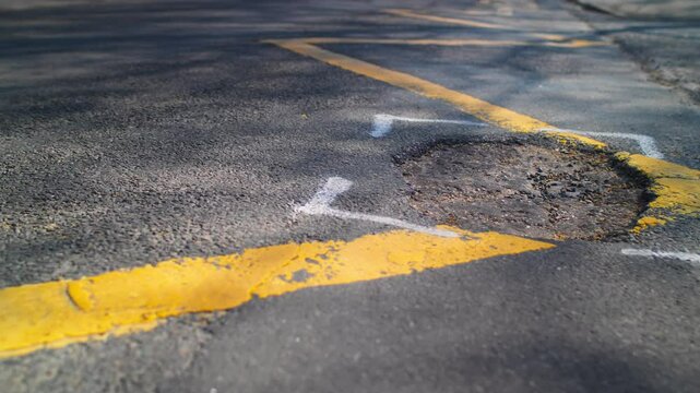 A large area of pothole tarmac damage in a suburban British street. The hole is highlighted for repair. 
