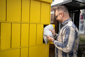 Man retrieving package from yellow delivery locker in a city setting during daylight hours