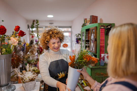 Cheerful florist shares vibrant flowers with a happy customer in a cozy shop