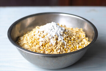 Cooked soybeans and tempeh starter in big bowl on white table close up, process of making tempeh, selective focus blur background