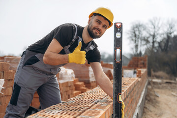 Using leveler tool. Construction worker is at job with bricks outdoors