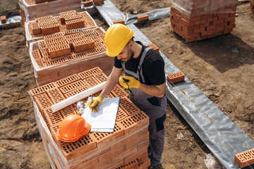Plan on the paper. Construction worker is at job with bricks outdoors