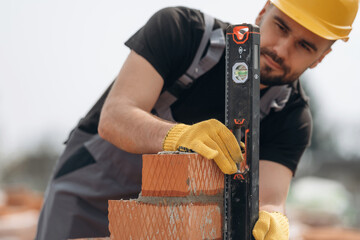 Using leveler tool. Construction worker is at job with bricks outdoors