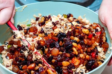 Hands mixing a colorful medley of fruit and nuts to make a delicious fruitcake from scratch.