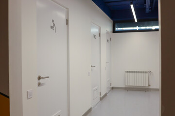 Modern public restroom corridor with white doors labeled 