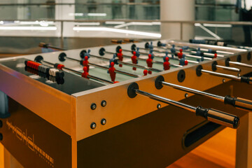 Obraz premium Modern foosball table with red and blue player figures in a brightly lit indoor setting, featuring sleek metal rods and wooden handles