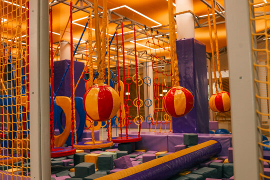 Colorful indoor obstacle course for kids with soft hanging balls, foam blocks, climbing rings, and safety nets in a brightly lit play area