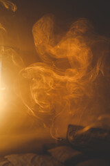Soft swirling smoke in warm golden light above a bed, creating a dreamy and abstract mood with smooth flow and ethereal atmosphere
