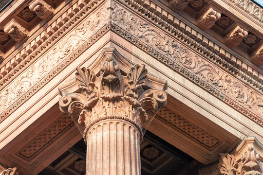 Close-up of a Corinthian-style column capital with elaborate carvings and detailed entablature from a classical architectural building