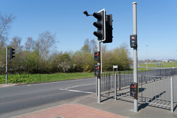 Multi level, standard, high and low, push button traffic lights for pedestrians, cyclists and horse riders next to a road with a blue sky in the distance.