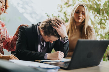 A stressed business professional sits at a desk with a laptop, comforted by supportive colleagues....