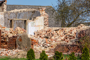 Ruins of a Brick Building. A partially collapsed brick building with rubble scattered around the site. abandoned and in a state of decay, surrounded by green grass and some small shrubs. A clear blue 