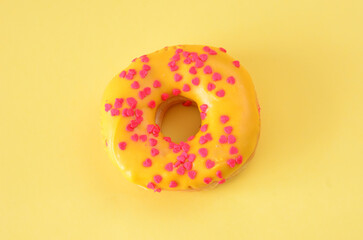 Delicious yellow donut with heart-shaped sprinkles on yellow background