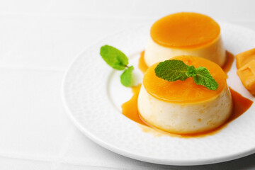 Tasty puddings with caramel sauce served on white tiled table, closeup. Space for text
