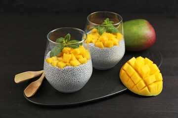 Delicious chia pudding with mango and mint in glasses on dark wooden table