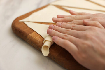 Woman rolling croissant from fresh dough at light table, closeup