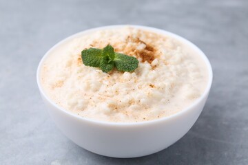Tasty rice pudding with cinnamon and mint in bowl on grey table, closeup