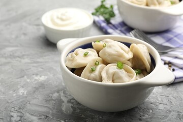 Delicious dumplings (pelmeni) with green onion in bowl on grey table, closeup
