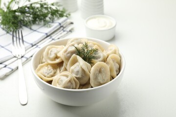 Tasty dumplings and dill in bowl on white textured table, closeup