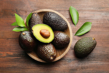 Fresh ripe avocados and leaves on wooden table, flat lay