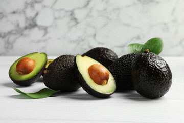 Whole, cut avocados and leaves on white wooden table against marble background, closeup
