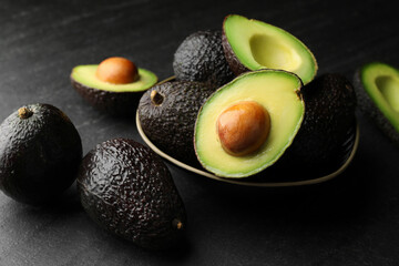 Whole and cut avocados on dark textured table, closeup