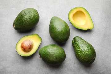 Many whole and cut avocados on light grey table, flat lay