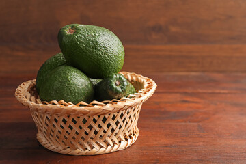 Whole avocados in wicker basket on wooden table, closeup. Space for text