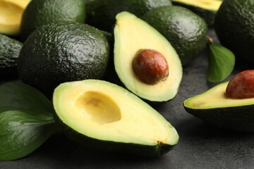 Whole and cut avocados on grey textured table, closeup