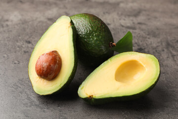 Whole and cut avocados on grey textured table, closeup